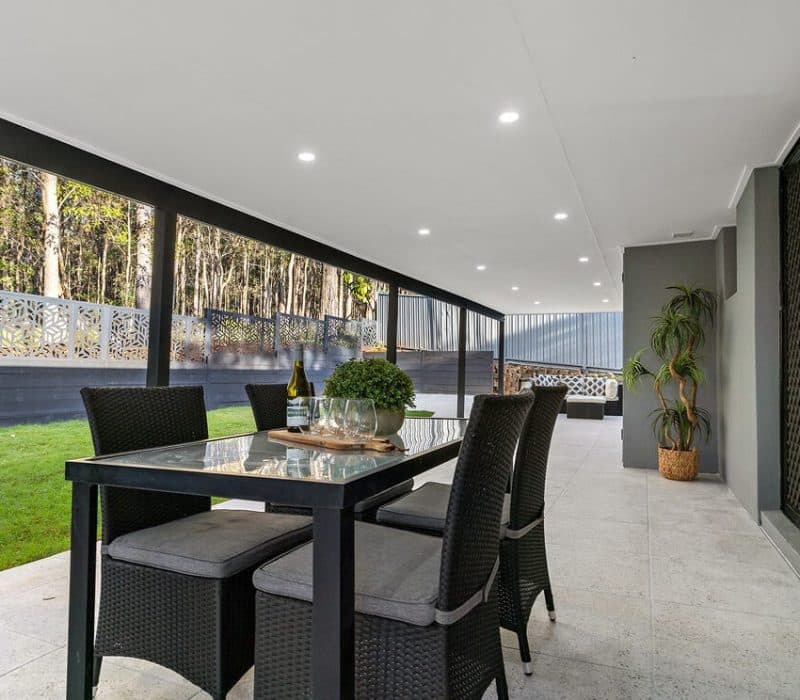 Covered alfresco dining area with screen panels and trees beyond