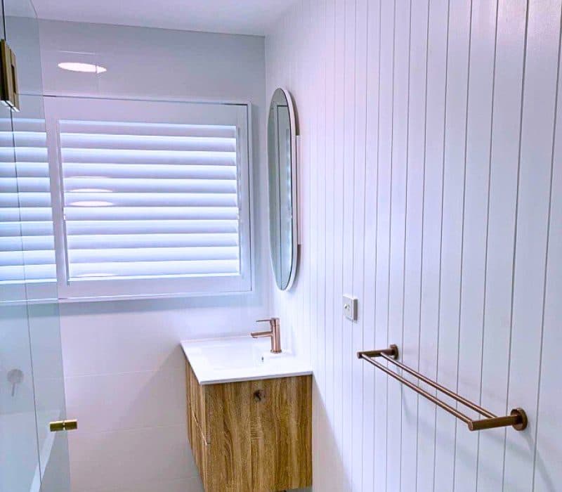 White bathroom with timber vanity and brass tapware at Mt Gravatt